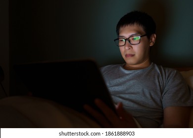 An Asian man between the ages of 35 and 40 plays a laptop in his bed. Concept of technology, poor health, insufficient rest - Powered by Shutterstock