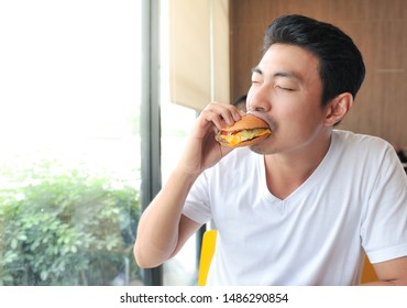 Asian Man Is Biting A Burger,A Man Enjoy Eating With Burger In His Hand,Burger Is Hight Calories Food,Selective Focus