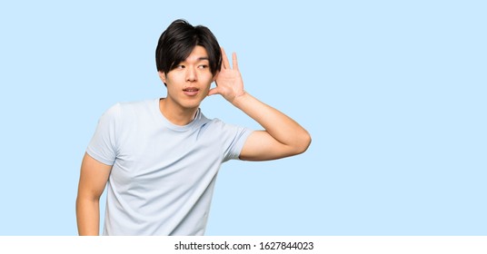 Asian man with blue shirt listening to something by putting hand on the ear over isolated blue background - Shutterstock ID 1627844023