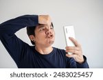 Asian man in a blue t-shirt is holding a cell phone and talking with a sense of humor