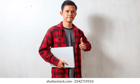 Asian man carrying laptop giving thumbs up ok symbol wearing checkered shirt isolated on white background - Powered by Shutterstock