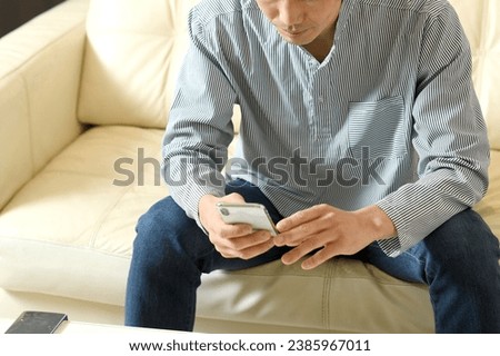 Asian man in casual clothes looking at his smartphone with a serious expression
