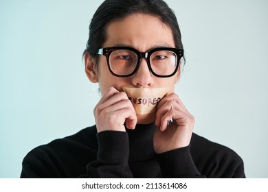 Asian man with censored sign on his lips holding ands near his face