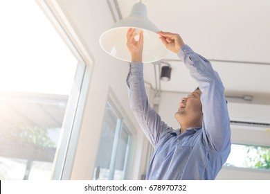 Asian Man Changing Light Bulb In Coffee Shop , Installing A Fluorescent Light Bulb