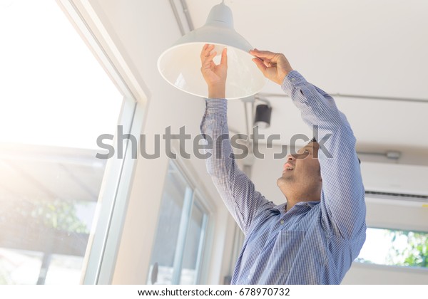 Asian man changing light bulb in coffee shop ,
installing a fluorescent light
bulb