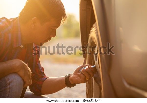 Asian man checking\
air pressure and filling air in the tires of his car. Car\
maintenance before driving\
concept