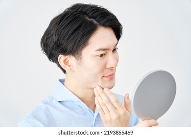 Asian Man Checking His Face With A Hand Mirror At Home