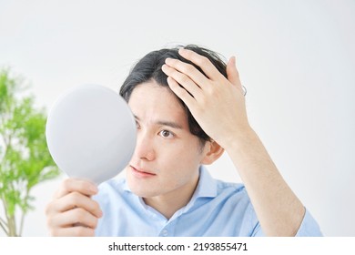 Asian Man Checking His Hair With A Hand Mirror At Home