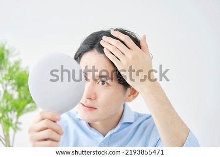 Asian man checking his hair with a hand mirror at home
