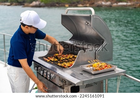 Asian man chef cooking grilled barbecue and seafood on stove for serving to passenger tourist travel on luxury private catamaran boat yacht on summer vacation. Cruise ship service occupation concept.