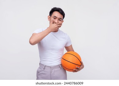 An Asian man chuckles while playfully covering his mouth, holding a basketball against a white background.