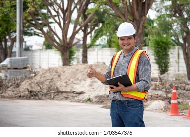 Asian man civil construction engineer worker or architect with helmet and safety vest working and holding a touchless tablet computer for see blueprints or plan at a building or construction site