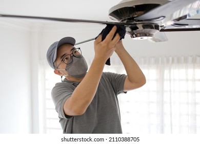 An Asian Man Cleaning Ceiling Fan At Home. Copy Space.