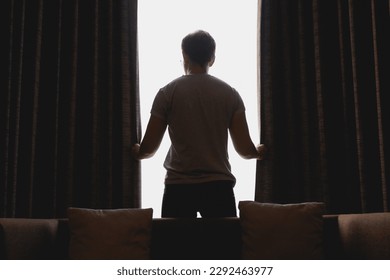 Asian man closing the curtain while watching the view out of the window. - Powered by Shutterstock