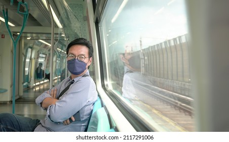 Asian Man Commuter With Face Mask On Inside A Moving Subway Train. Masked Transit Concept.