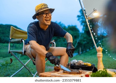 Asian man cooking meal grilled bbq steak for dinner party at camp at sunset. Group of People enjoy outdoor adventure lifestyle travel nature hiking and camping together on summer holiday vacation. - Powered by Shutterstock