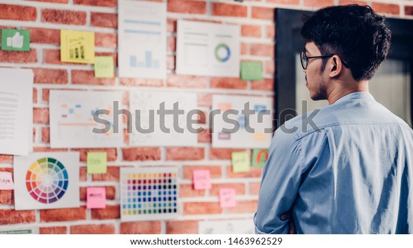 Asian man creative director designer looking at
data chart and find idea on brickwall at modern
office.brainstroming creative ideas
concpet