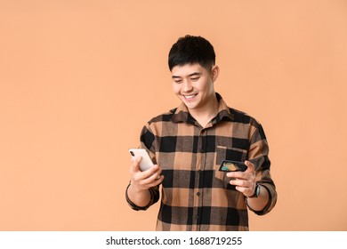 Asian Man With Credit Card And Mobile Phone On Color Background