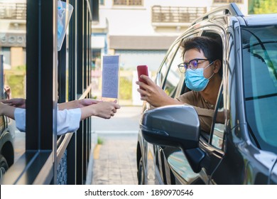 Asian man customer using mobile scan QR or NFC payment on smart phone paying for his coffee drink in coffee shop while he drive thru and Barista wearing mask in background
