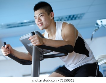 Asian Man Cycling On Exercise Bike In Gym