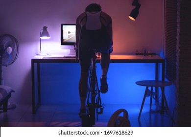 Asian Man Cycling On The Machine Trainer He Is Exercising In The Home At Night.he Play Online Bike Game 