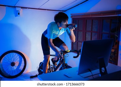 Asian Man Cycling On The Machine Trainer He Is Exercising In The Home At Night.he Play Online Bike Game 