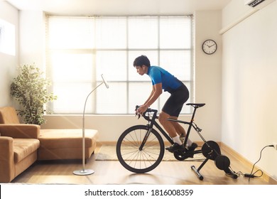 Asian man cyclist. he is exercising in the house and  trainer and play online bike games.He stood up spinning