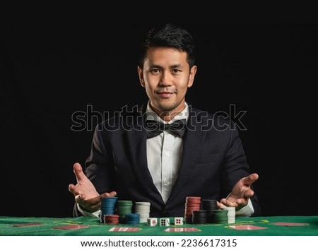 Asian man dealer or croupier shuffles poker cards betting in casino on black background of green table, Dealer man invitation bet playing cards. Casino, poker, poker game concept.