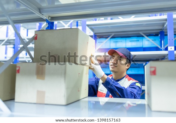 Asian man\
delivery staff in blue uniform work in warehouse keep goods, Auto\
mechanic is checking stock friendly worker in a warehouse and trade\
for car spare parts of a car repair\
shop.