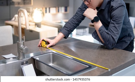 Asian Man Designer Using Tape Measure For Measuring White Granite Countertops On Modern Kitchen Counter In Showroom. Shopping Furniture Material For Home Improvement. Interior Design Concept