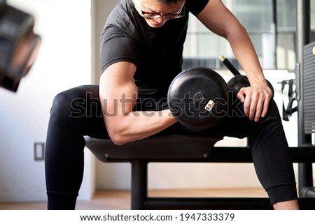 Asian man doing dumbbell curls in a training gym