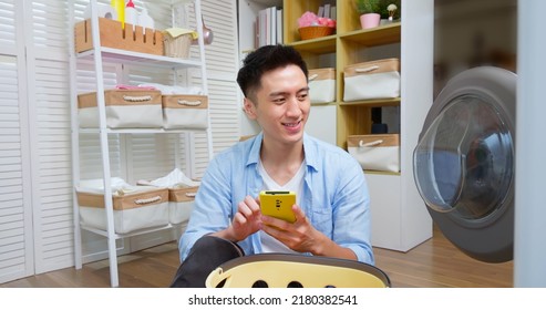 Asian Man Doing Laundry With Smartphone Controlling