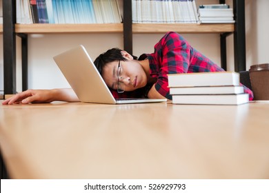 Asian man dressed in shirt in a cage and wearing glasses sleeping at the library near laptop and books. - Powered by Shutterstock