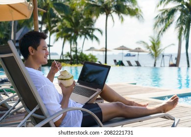 Asian Man Drinking Coconut Water While He Is Working On His Laptop On A Chairnear Pool At Resort Hotel On Summer Vacation Holiday.
