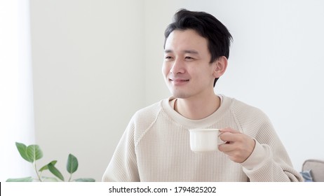Asian Man Drinking Coffee In The Living Room