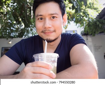 Asian Man Drinking Iced Green Tea At The Garden Of The Cafe.