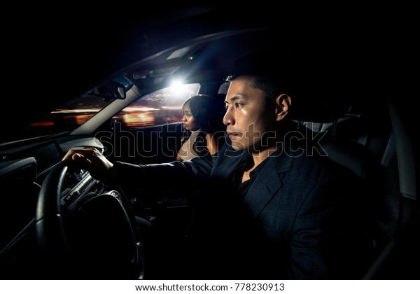 Asian man driving with a black african female\
date in a car.  They look like they are heading to a nightclub for\
clubbing nightlife.  The image depicts interracial relationships\
and lifestyle.