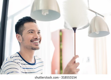 Asian Man Dusting His Home Using Duster On Lamp