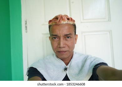 A Asian man dyeing his hair in yellow looking at the camera.