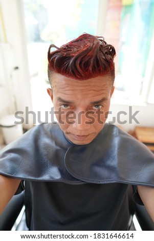 A Asian man dyeing his hair red looking at the camera