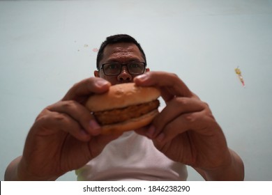 An Asian Man Eating Burger On Green Bright Background Photo. Self Potrait.