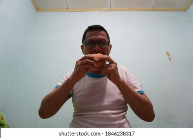 An Asian Man Eating Burger On Green Bright Background Photo. Self Potrait.