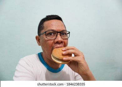 An Asian Man Eating Burger On Green Bright Background Photo. Self Potrait.