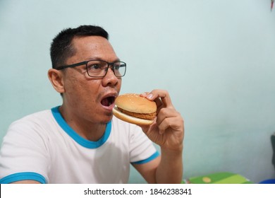 An Asian Man Eating Burger On Green Bright Background Photo. Self Potrait.