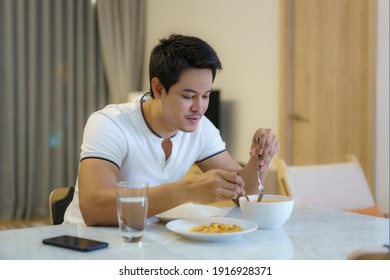 An Asian man is eating dinner alone at the dining table at night at home. - Shutterstock ID 1916928371