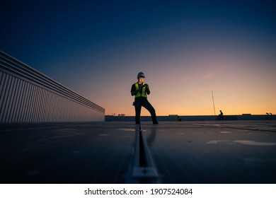 Asian Man Engineer Service Check Installation Solar Cell On The Roof Of Factory On The Morning. Silhouette Technician With Solar Cell On The Roof Of Factory Under Morning Sky. Technology Solar Cell.