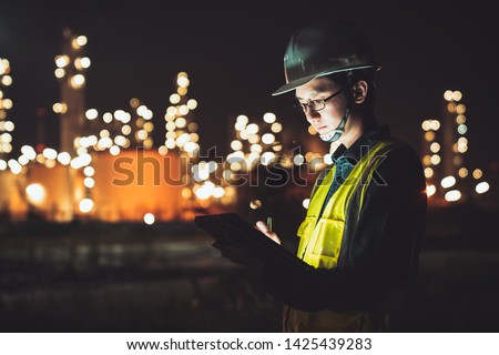 Asian man engineer using digital tablet working late night shift at petroleum oil refinery in industrial estate. Chemical engineering, fuel and power generation, petrochemical factory industry concept