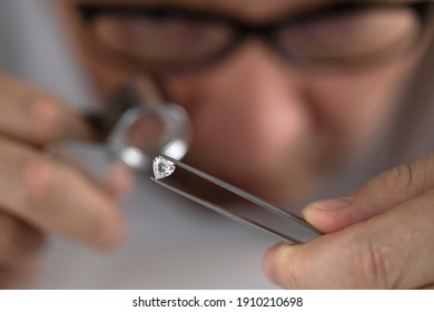 Asian man expert buyer with glasses evaluates polished diamond trough magnifying glass close up. 