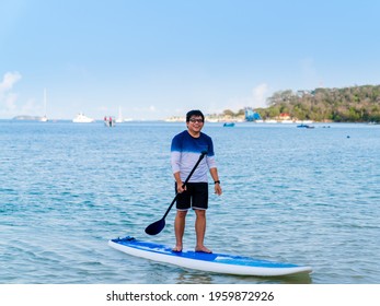 Asian Man With Eyeglasses In Casual Clothes Standing On Stands Up Paddleboard, Man Happy Smiling Paddleboarding On Blue Sea Water On Summer Holiday In Thailand Beach