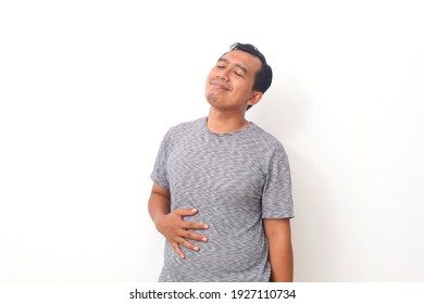 Asian Man Feel Very Full After Eating Too Much Food. The Man Holds His Stomach Full Of Food. Isolated On White Background